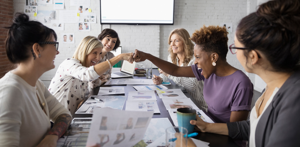 Female designers fist bumping in conference room meeting
